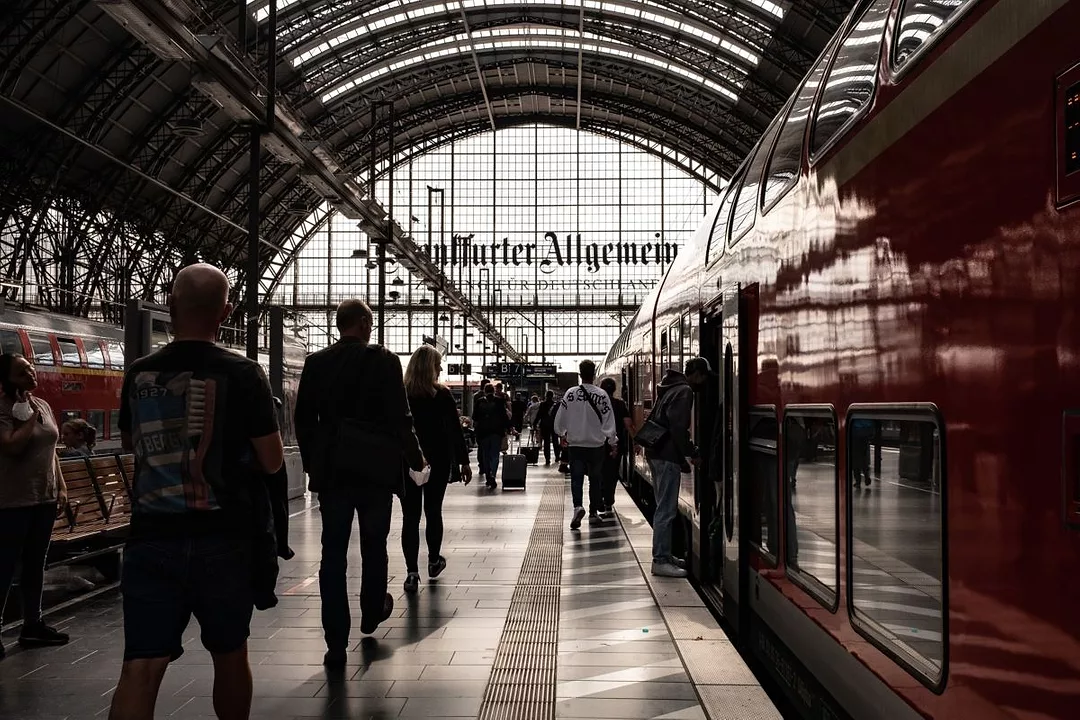 RAIL PASSENGERS SILHOUETTED AGAINST THE GLASS STRUCTURE OF A RAILWAY STATION