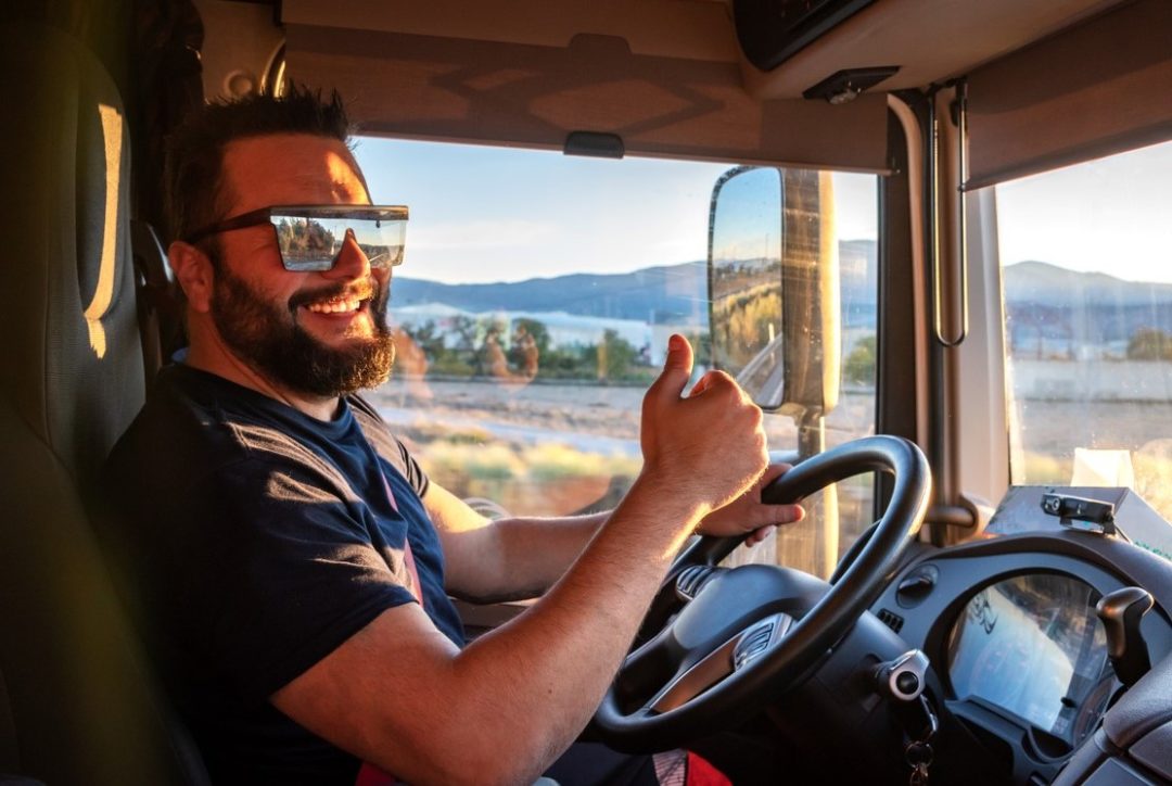 A DRIVER IN A TRUCK CAB GIVES A THUMBS-UP SIGN, SMILING