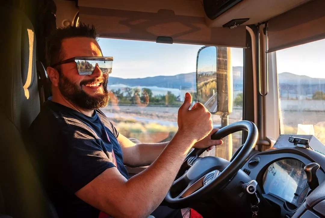 A DRIVER IN A TRUCK CAB GIVES A THUMBS-UP SIGN, SMILING