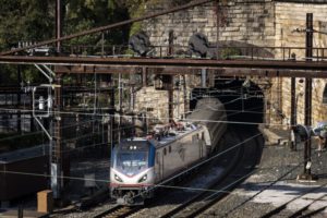 AN AMTRAK TRAIN EMERGES FROM A TUNNEL, THE AIR ABOVE IT STREWN WITH WIRES