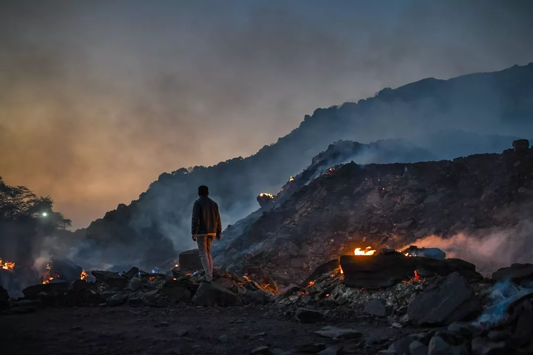 A LONE FIGURE WALKS AMONG SMOKING PILES OF COAL SLAG
