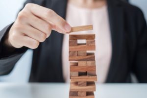A WOMAN IN A SUIT, BLURRED IN THE BACKGROUND, MOVES A PIECE ON TOP OF A JENGA TOWER