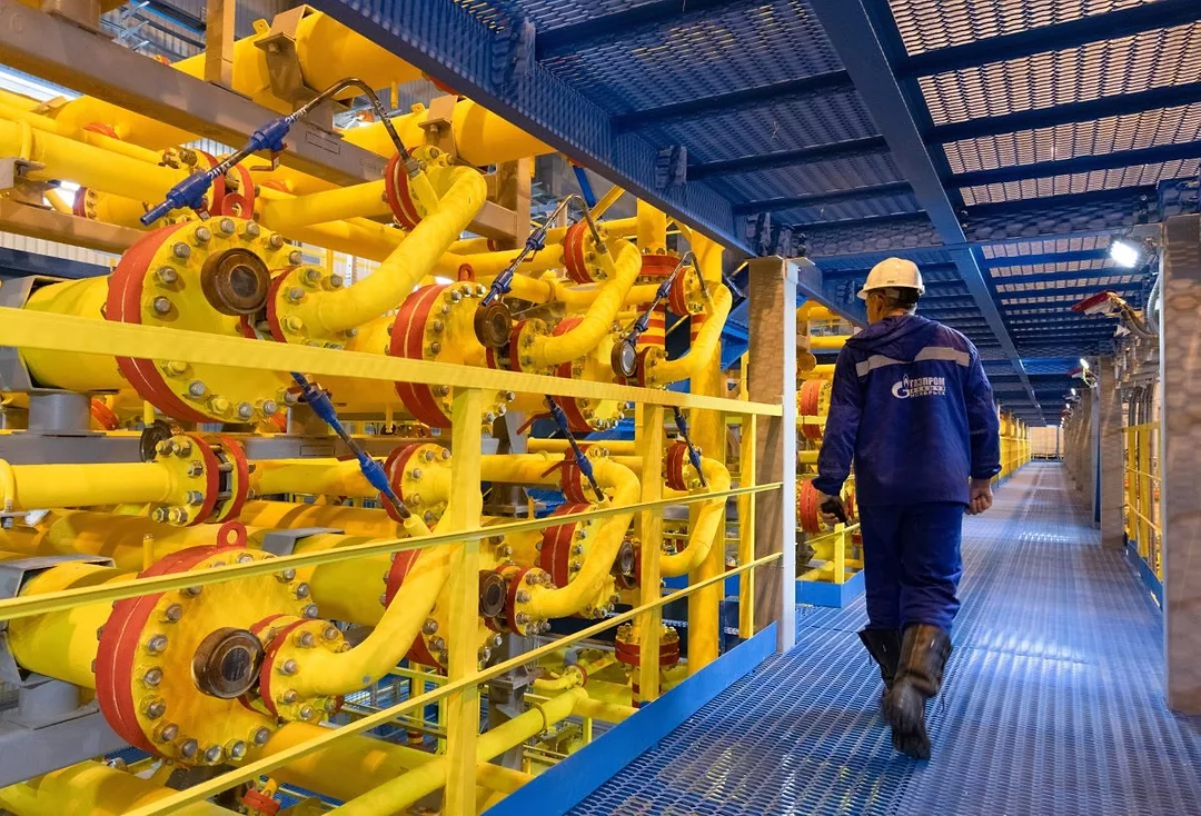 A WORKER ON A METAL WALKWAY PASSES BRIGHT YELLOW OIL PIPES IN A REFINERY