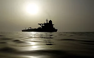 AN OIL TANKER ON A SMOOTH SEA SPOUTS SMOKE INTO THE AIR