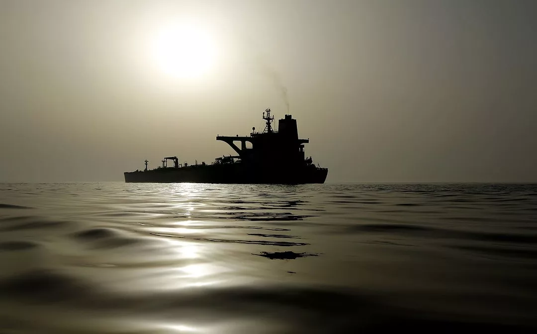 AN OIL TANKER ON A SMOOTH SEA SPOUTS SMOKE INTO THE AIR