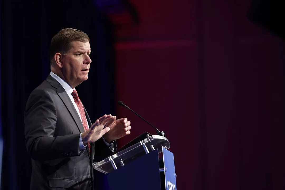 A MAN IN A DARK SUIT SPEAKS AT A PODIUM