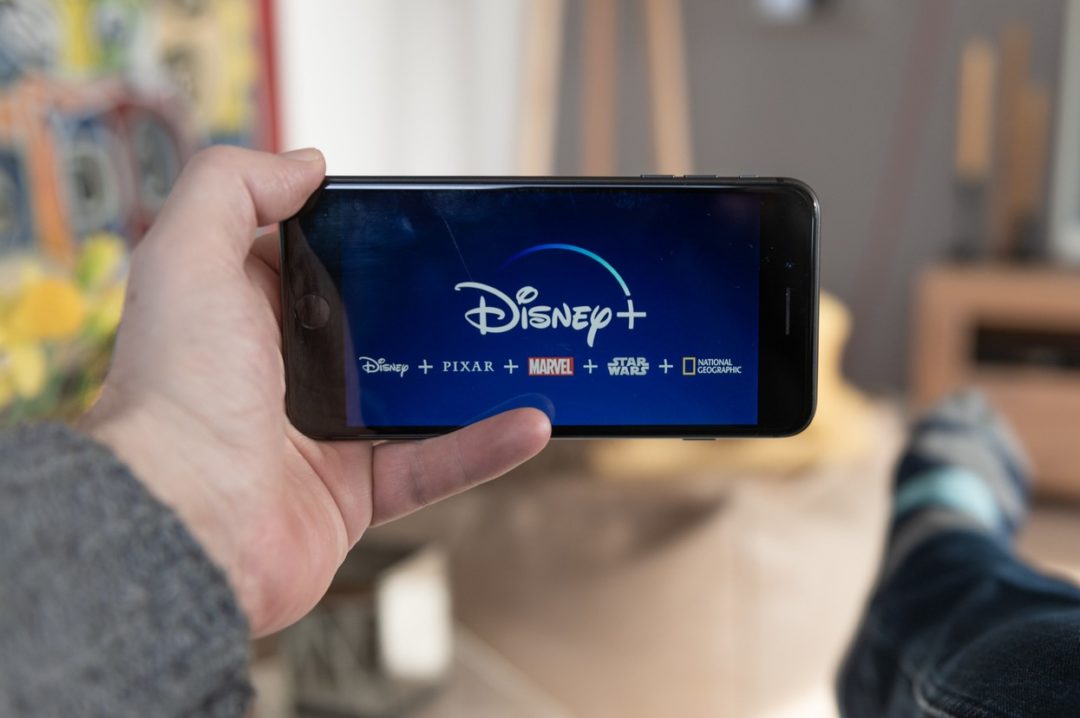 A HAND HOLDS UP A SMARTPHONE STREAMING CONTENT WITH THE DISNEY LOGO