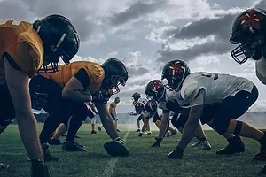 FOOTBALL PLAYERS CROUCH ON A PLAYING FIELD, READY TO PLAY