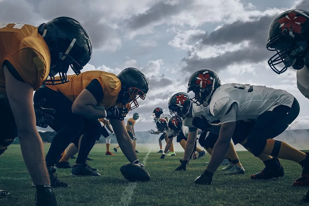 FOOTBALL PLAYERS CROUCH ON A PLAYING FIELD, READY TO PLAY