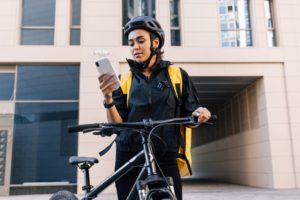 A young courier in a bike helmet checks her smartphone.