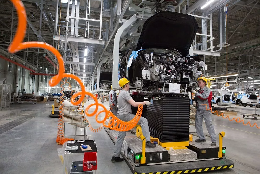 TWO WORKERS TEND A CAR ON AN ASSEMBLY LINE
