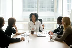 Black female boss leading corporate meeting talking to diverse businesspeople 