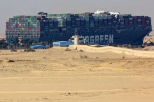 BEYOND SAND DUNES AND BUILDINGS, A HUGE CONTAINER SHIP LOOMS UNCOMFORTABLY CLOSE