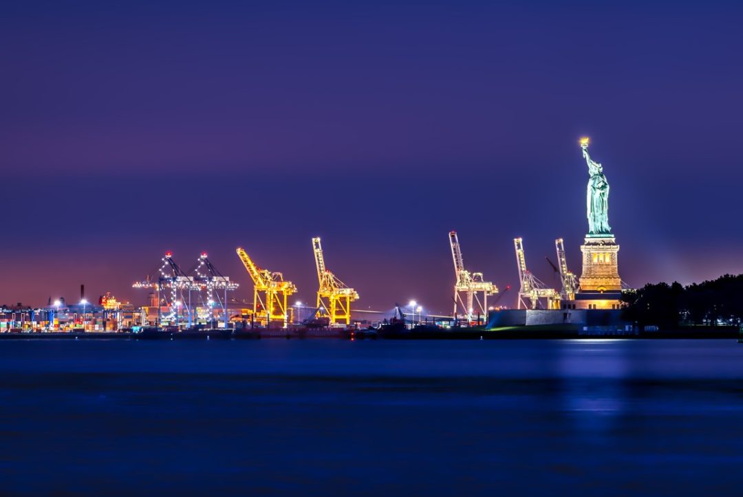 The Statue of Liberty overlooking port Cranes, all lit up, at night