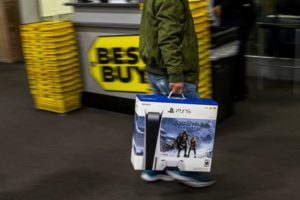 A SHOPPER CARRIES A LARGE BOX CONTAINING A PLAYSTATION OUT OF A BEST BUY STORE