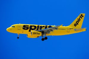 A BRIGHT YELLOW SPIRIT AIRLINES PLANE FLIES IN AN ELECTRIC BLUE SKY