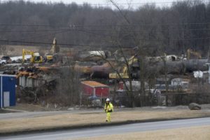 A WORKER IN HI-VIS YELLOW SUIT WALKS PAST A PILE OF TRAIN WRECKAGE