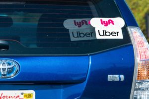 A BLUE CAR'S REAR WINDOW BEARS BOTH UBER AND LYFT STICKERS