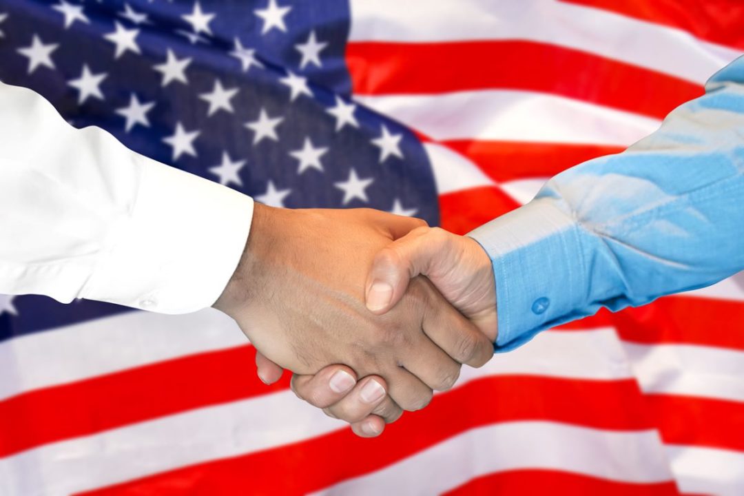 TWO HANDS IN SHIRT CUFFS SHAKE AGAINST A BACKGROUND OF A US FLAG