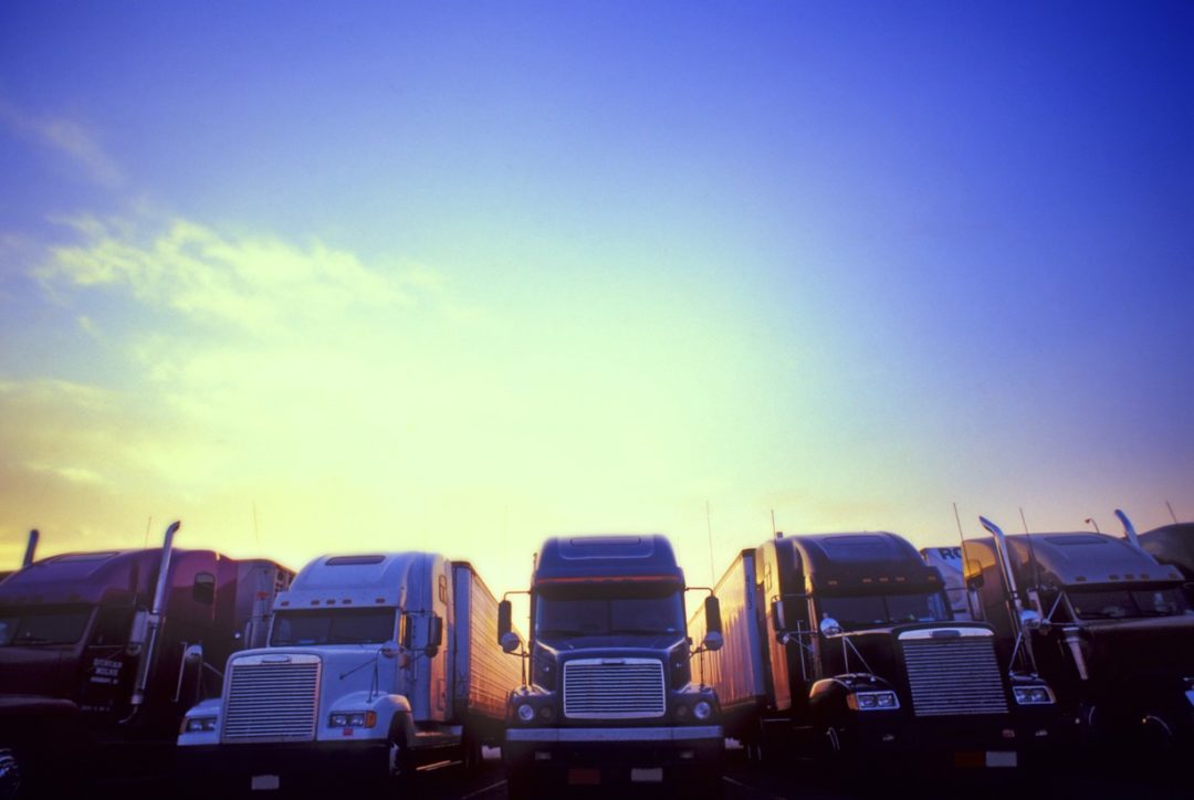 A ROW OF TRUCKS STANDS AGAINST A SUNSET SKY