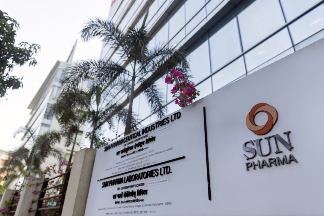 A SIGN BEARS THE SUN PHARMA LOGO OUTSIDE A GLASS OFFICE BUILDING FRINGED WITH PALM TREES