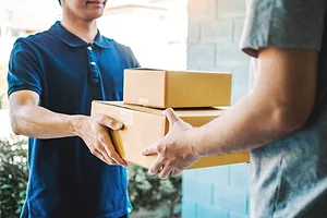A HOME DELIVERY DRIVER HANDS BOXES TO A CONSUMER AT THEIR DOORSTEP39.jpg