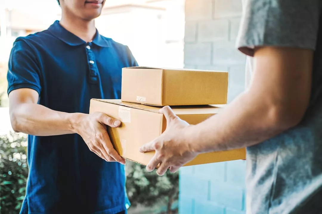 A HOME DELIVERY DRIVER HANDS BOXES TO A CONSUMER AT THEIR DOORSTEP39.jpg