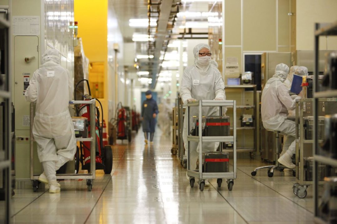 WORKERS IN HYGIENE OVERALLS AND MASKS OPERATE IN A HI-TECH FACTORY