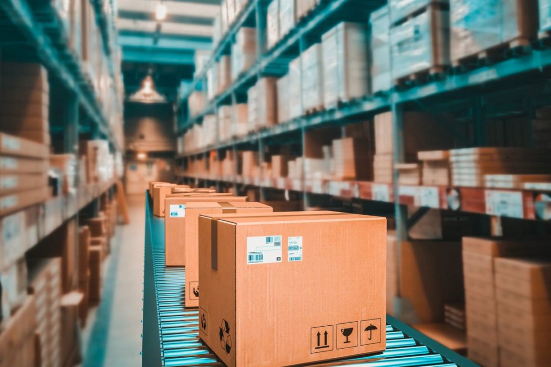 A LINE OF PARCEL BOXES PROGRESSES ALONG A CONVEYOR IN A WAREHOUSE