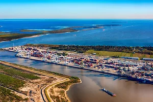 A CARGO SHIP MAKES IT WAY OUT OF THE CHANNEL OF A PORT TOWARD THE OPEN SEAS