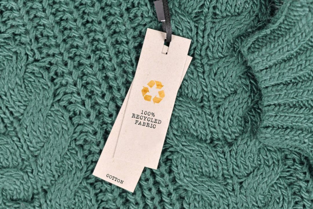 A LABEL ON A DARK GREEN CABLE KNIT SWEATER READS 100% RECYCLED FABRIC