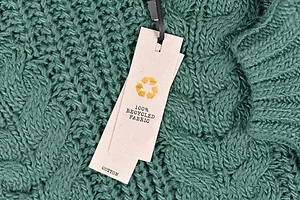 A LABEL ON A DARK GREEN CABLE KNIT SWEATER READS 100% RECYCLED FABRIC