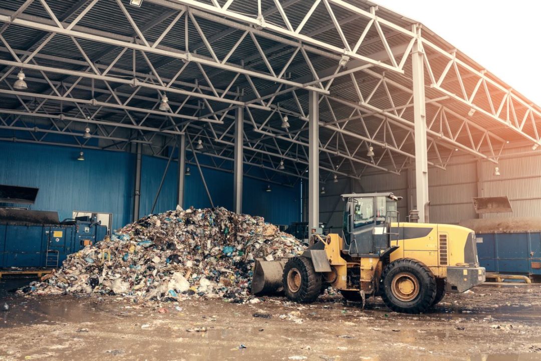 A BULLDOZER MOVES PILES OF DISCARDED MATERIALS UNDER THE AWNING OF A DEPOT
