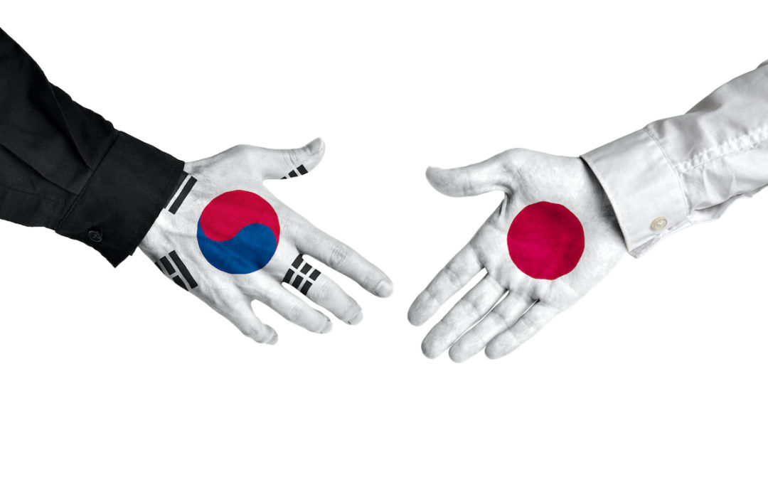A diplomatic handshake is taking place between two individuals with the flags of South Korea and Japan painted on their hands. The left hand is South Korea. The right hand is Japan. Photo: iStock.com/Kagenmi