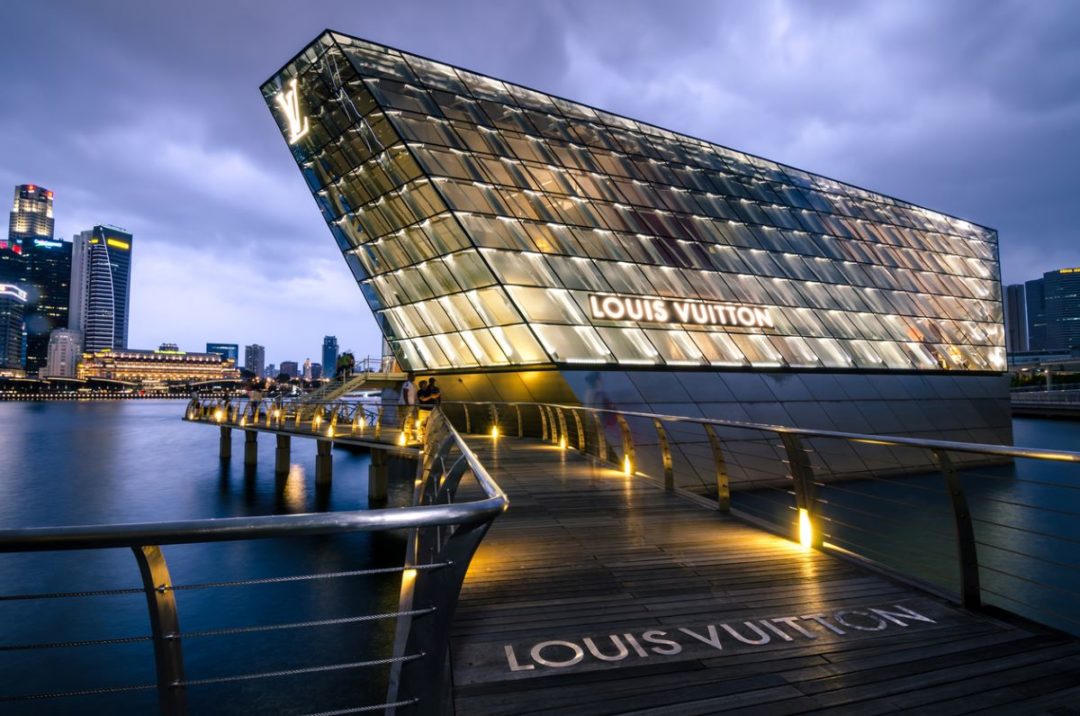 AN ULTRA-MODERNIST GLASS AND STEEL BUILDING BEARING THE LOUIS VUITTON INSIGNIA LOOMS OUT OVER A BAY