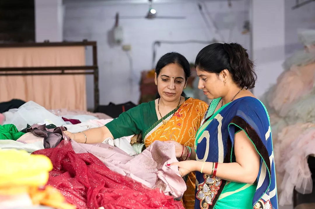 TWO GARMENT FACTORY WORKERS WEARING SARIS HOLD A STACK OF CLOTH PIECES