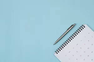 A calendar with a pen above it rests on top of a blue background. Photo: iStock.com/Rattankun Thongbun