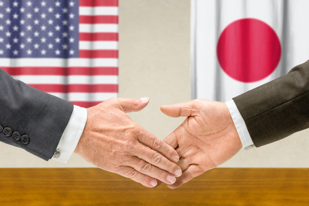 A handshake is taking place between two people with the flags of the United States and Japan in the background. Photo: iStock.com/Zerbor