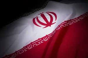 A CLOSE UP PHOTO OF THE CENTER OF THE FLAG OF IRAN, BEARING THE COAT OF ARMS OF IRAN