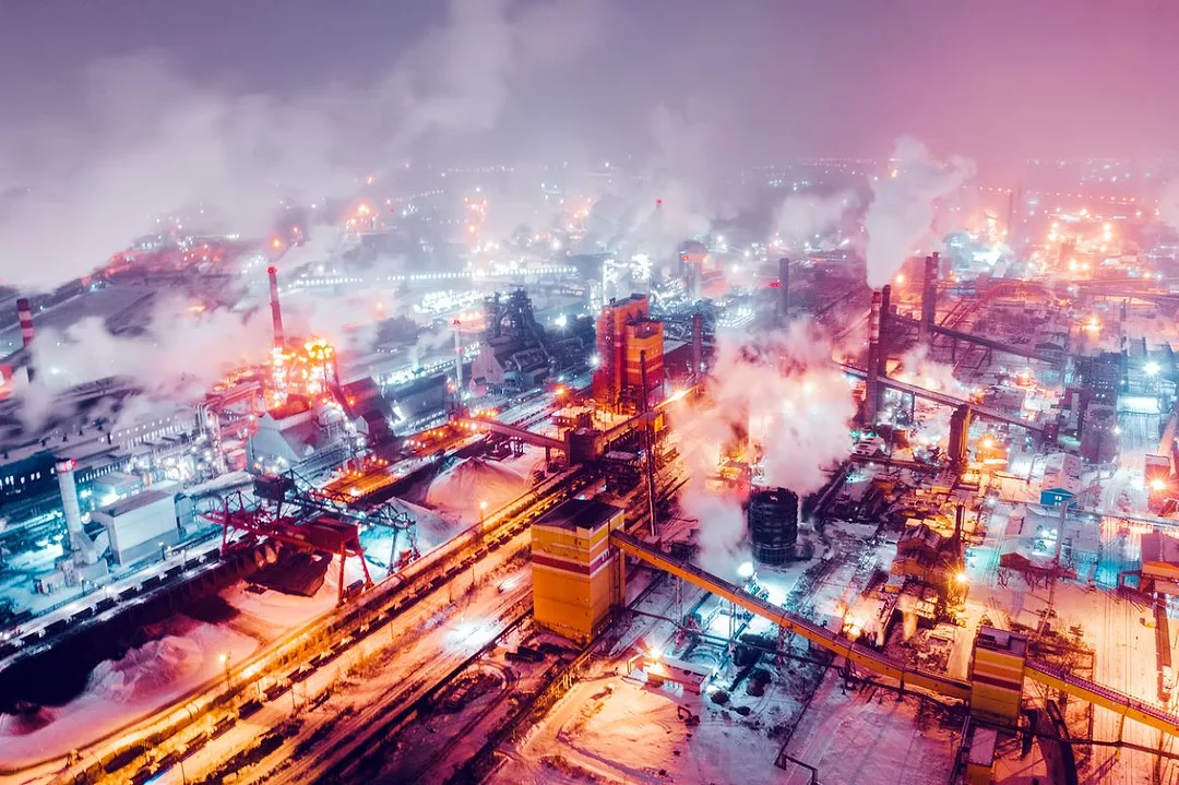 Aerial view of steel plant at night with smokestacks and fire blazing out of the pipe.