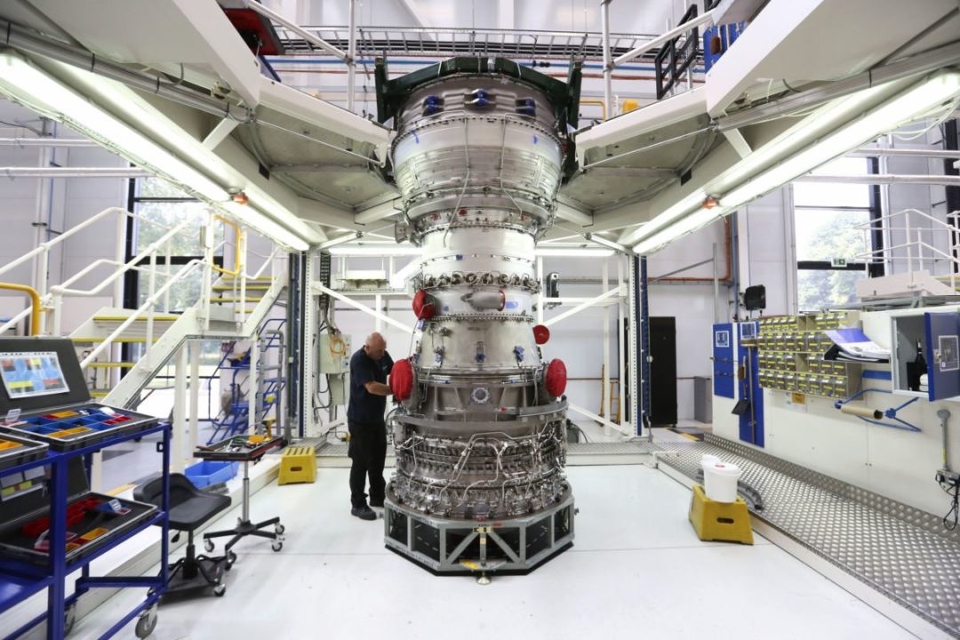 AN ENGINEER TENDS A GIANT AIRCRAFT ENGINE IN A SUPER-CLEAN MANUFACTURING AREA