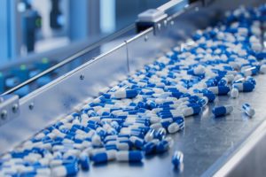 A STREAM OF BLUE AND WHITE DRUG CAPSULES FLOWS THROUGH A PHARMACEUTICAL MANUFACTURING PLANT
