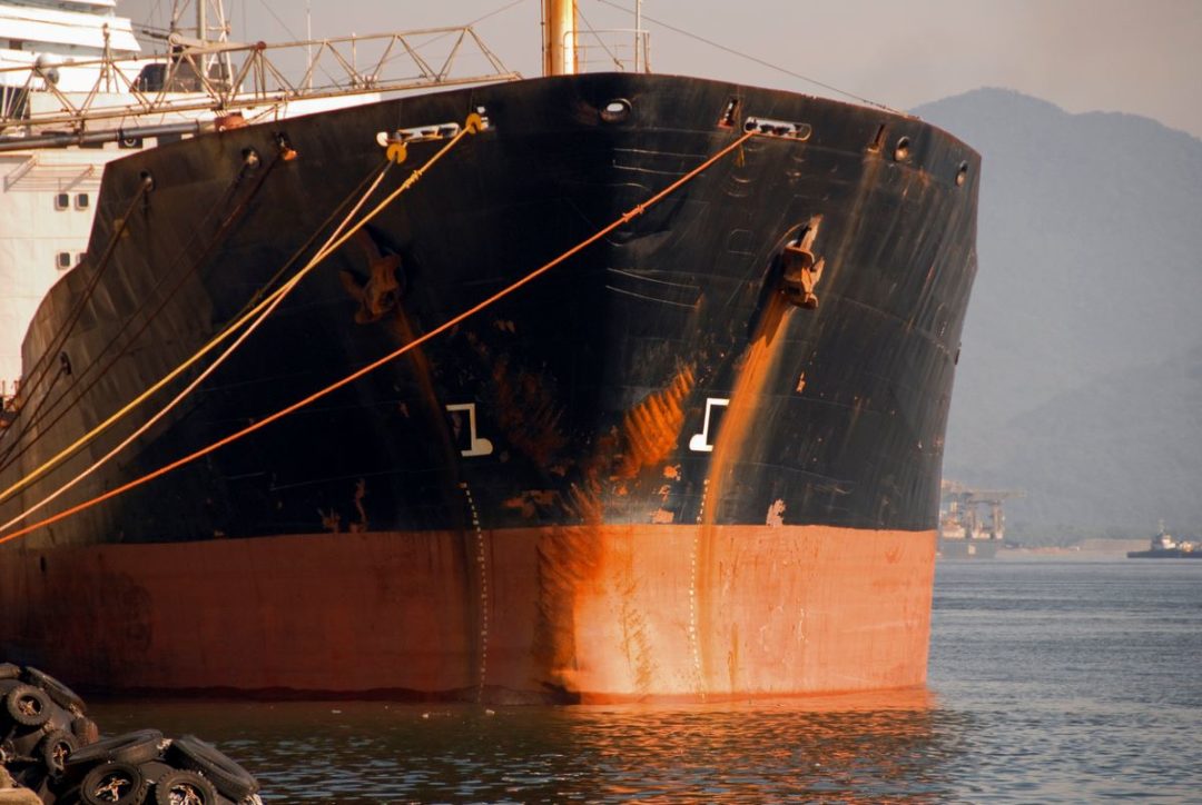 AN OIL TANKER WITH VISIBLE SIGNS OF RUST, SEEN AT WATER LEVEL ENTERING A PORT