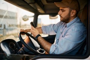 A TRUCK DRIVER LOOKS AT A CELLPHONE WHILE CLUTCHING THE WHEEL