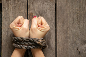 A PAIR OF FEMALE HANDS ARE TIED UP IN FRONT OF A WOODEN BACKGROUND.