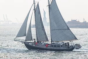 A SCHOONER SAILING BOAT PASSES THE STATUE OF LIBERTY ON A BRIGHT, BREEZY DAY