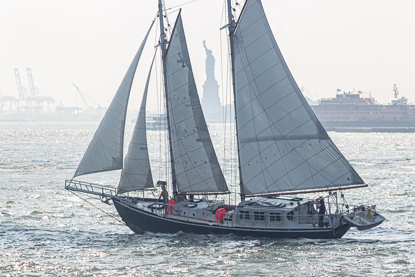 A SCHOONER SAILING BOAT PASSES THE STATUE OF LIBERTY ON A BRIGHT, BREEZY DAY