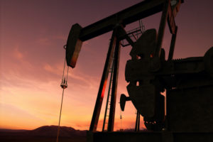 A PUMP JACK OIL RIG IS OPERATING AS THE SUN SETS.