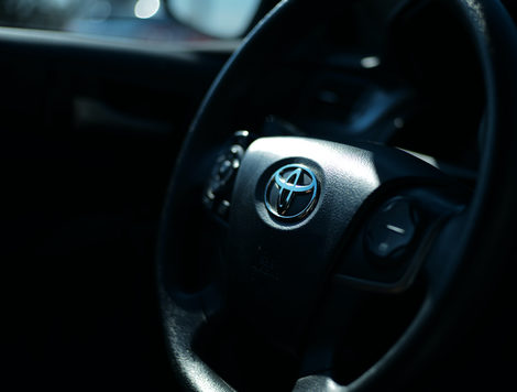 THE BLACK INTERIOR OF A CAR SHOWS A BLACK STEERING WHEEL WITH A TOYOTA LOGO IN THE CENTER OF IT.