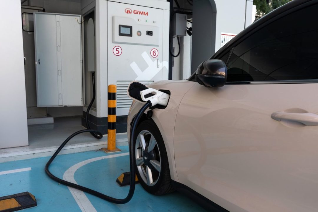 A WHITE ELECTRIC VEHICLE IS PLUGGED INTO A GWM CHARGING STATION.